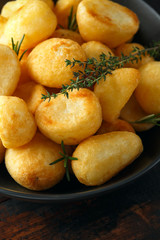 Roast golden potatoes seasoned with salt, garlic, rosemary and thyme on rustic wooden background