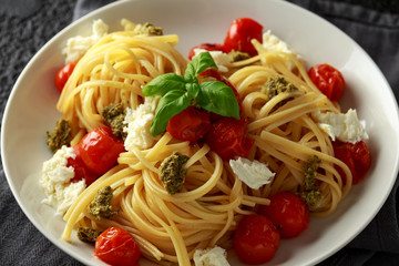 Pasta with green pesto sauce, roasted cherry tomatoes and mozzarella cheese in white plate on dark rustic background