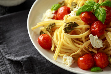 Pasta with green pesto sauce, roasted cherry tomatoes and mozzarella cheese in white plate on dark rustic background
