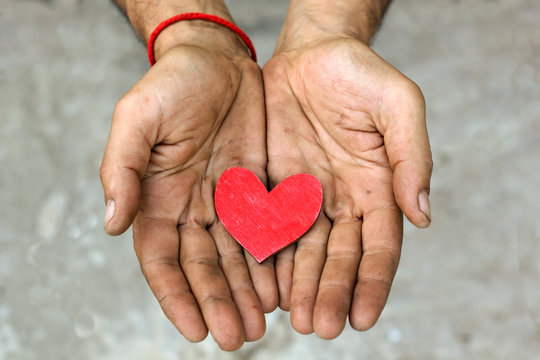 Man holding red wooden heart in dirty hands