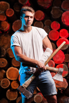 Close-up of a lumberjack worker with an axs in his hands against the background of firewood  