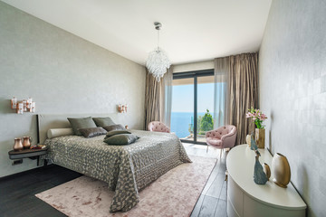 Interior of a spacious light bedroom with windows in a luxury villa. Big comfortable double bed in elegant modern bedroom