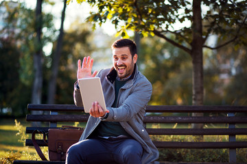 Fototapeta premium Businessman make video call using digital tablet while sitting on a bench in a park