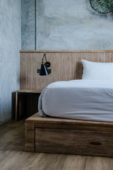 Neutral bedroom interior, light wooden bedhead, grey concrete wall, white bed sheets. Minimal loft design