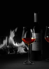 Stilleben mit einer Flasche und einem Glas Rotwein im Bordeaux Stil vor gemütlichem Kamin Feuer