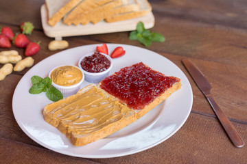 Creamy peanut butter toast and strawberry jam toast on plate with nut and fruit.