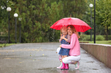 Happy mother and daughter with red umbrella in park on rainy day. Space for text