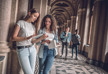 We are good team! Two beautiful students in the university looking at the tablet preparing for...