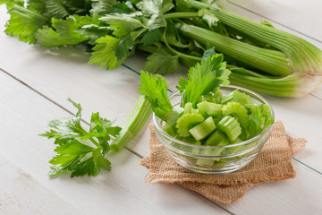 Fresh celery sliced in bowl with bunch celery on white wood background.