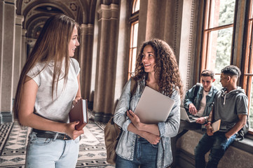 Friends and study partners! Group of college students standing together and chatting on the university hall.