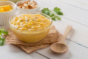 Corn soup in glass bowl and crispy bread with corn on white table.