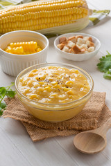 Corn soup in glass bowl and crispy bread with corn on white table.