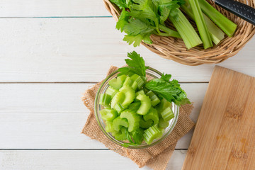 Fresh celery sliced in bowl with bunch celery on white wood background. Top view and Copy space.