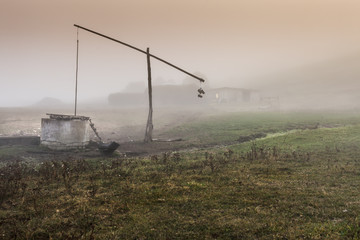 Small lonely provincial  farm with weel pole weel on a foggy morning near Sic village, Transylvania, Romania