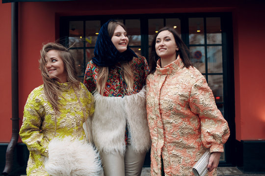 Three young stylish women are smiling and walking down the street.