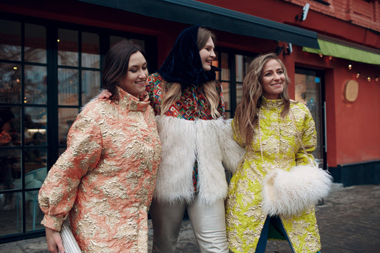 Three young stylish women are laughing and walking down the street.