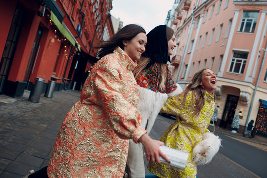 Three young stylish women are laughing and walking down the street.