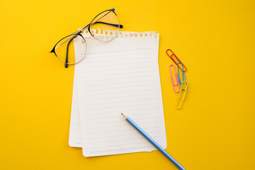 empty paper of notebook eyeglasses and pencil on color background.