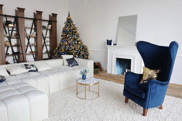  luxury apartment  decorated for New Year with white walls, christmas tree with gold and blue bolls, fireplace, dark blue velvet style chair