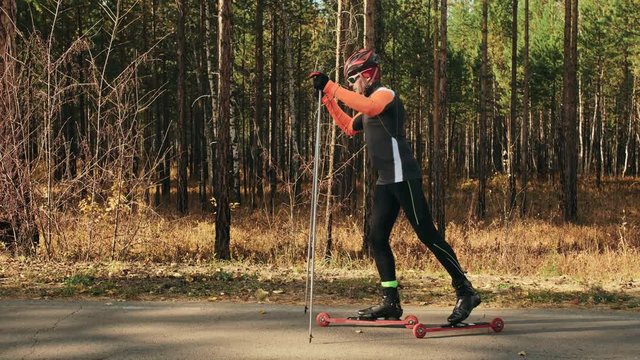 Training an athlete on the roller skaters. Biathlon ride on the roller skis with ski poles, in the helmet. Autumn workout. Roller sport. Adult man riding on skates. The athlete shows the basics of