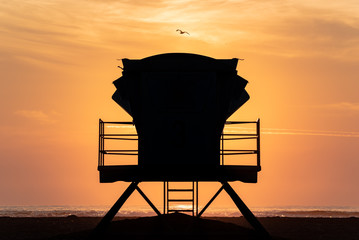Silhouette of a lifeguard tower on the beach surrounded by the orange sky of the sunset.