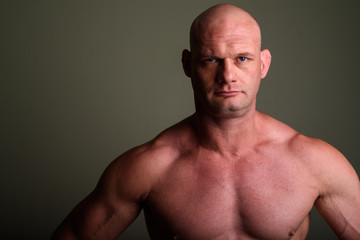 Bald muscular man shirtless against colored background