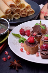 Rolled crepes with chocolate paste topped with raspberries, pomegranate, mint and chocolate pieces on a white plate