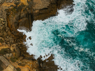 Aerial top view of sea waves hitting black volcanic rocks on the coastline with turquoise sea water. Amazing rock cliff seascape in the Portuguese coastline.