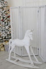 Children's wooden white horse rocking chair next to the Christmas tree in an apartment decorated for New Year