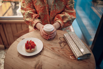 A young woman is sitting in a pastry shop cafe with coffee and cake.