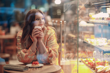 A young woman is sitting in a pastry shop cafe with coffee and cake.