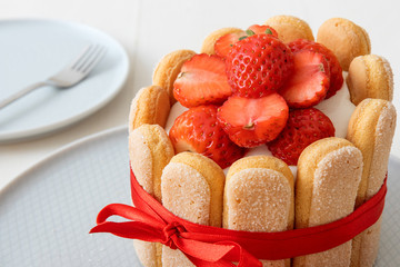Charlotte, French dessert with strawberries, tied up with a scarlet ribbon, coffee cup, bowl with strawberries on white table.