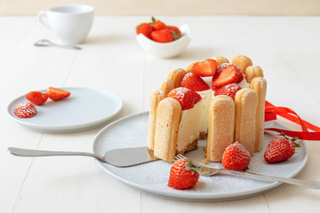 Charlotte, French dessert with strawberries, tied up with a scarlet ribbon, coffee cup, bowl with strawberries on white table.