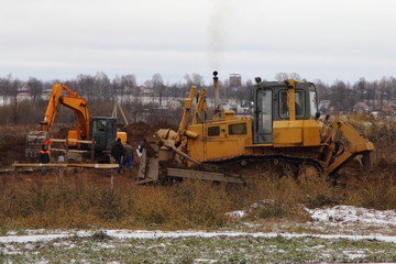 Yellow bulldozer equates land with a scraper on the background of the excavator earthworks, landscaping, construction site