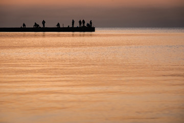 Silhouette of people fisherman on pier while beautiful sea sunset or dawn. Focus is on people