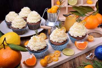 Cupcakes topped with butter cream, slices of kumquat and rosemary surrounded by fruits. Christmas dessert