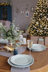 Elegant Christmas tree with gifts in the living room with dinner table near the textured gray walls in luxury apartments. 