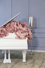 white grand piano decorated with pink pale yellow peonies made of paper in luxury suites with gray walls and a silver lamp