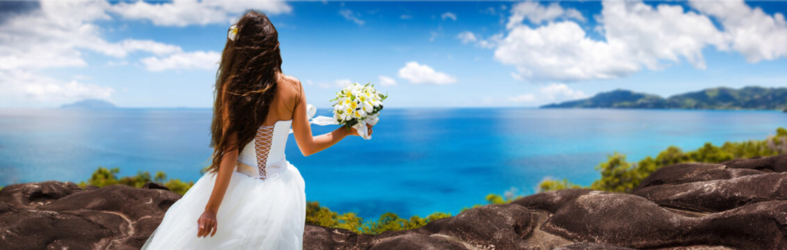 bride, beautiful young girl with dark hair in a white wedding dress with bouquet on  background of beach with blue water. Seychelles