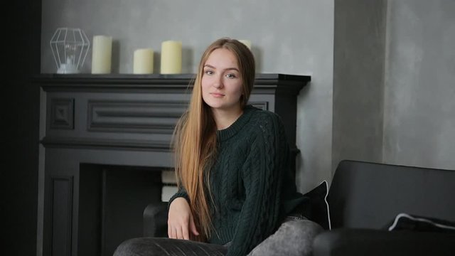young beautiful woman, girl sitting on the couch on the background of the fireplace with candles looking at the camera and calling on your smartphone.