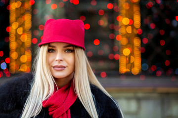 Pretty blonde model wearing funny red cap and scarf posing at the garlands blurred background