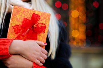 Attractive blonde girl with long hair wearing fur coat holding gift box. Space for text