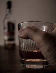 a grabbed glass of whisky and bottles on wooden table