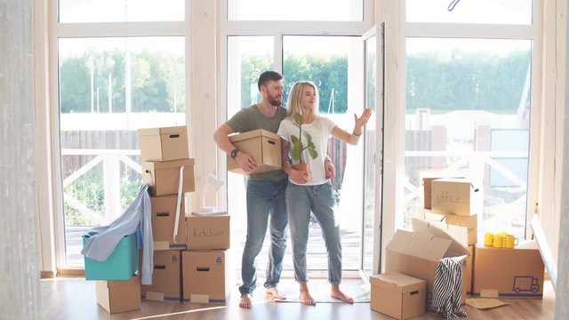 Moving to new home. Happy couple holding cardboard boxes while going into the house