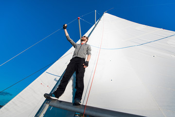Young seaman on a sailboat standing on a sail boom. Captain of the yacht in the open sea.