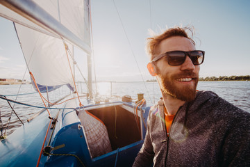 Man dressed in casual wear and sunglasses on a yacht. Happy adult bearded yachtsman close-up...