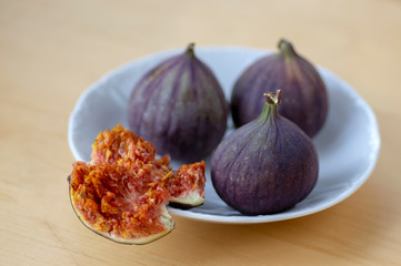 Common fig Ficus carica ripened violet fruits, group of figs on small white plate on wooden table