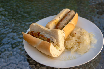 German sausages called bratwursts roasted in baguette with mustard, onion and pickled sauerkraut on white plate in Bosna style