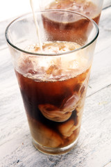 Ice coffee on a rustic table with cream being poured into it showing the texture and refreshing look of the drink
