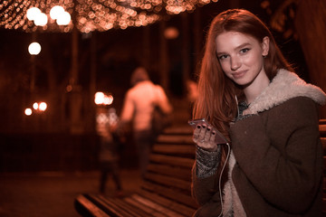 The portrait of an young smiling redhear lady on the evening listening musik